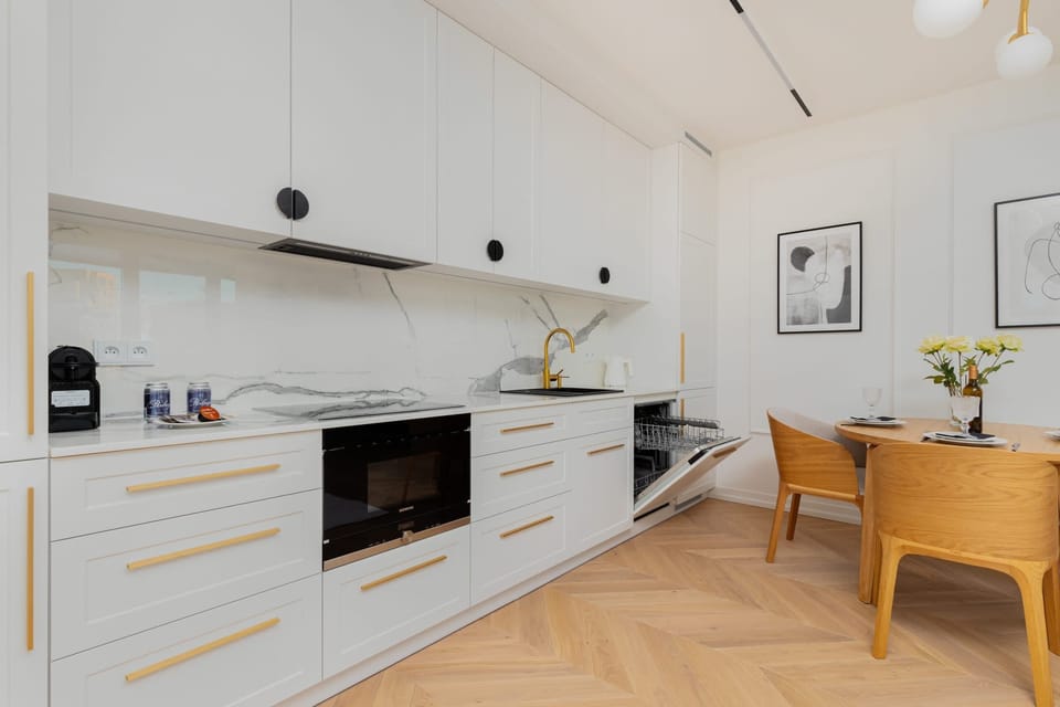 Dining table and chairs located next to the functionally equipped kitchenette with a dishwasher, kettle, and microwave.