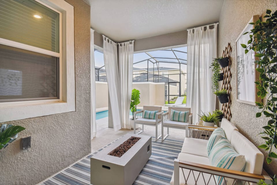 Welcome to our delightful outdoor lounge, where sunlight filters through sheer curtains, creating a serene atmosphere. Relax in cozy seating by the firepit, embraced by lush greenery for a refreshing escape.