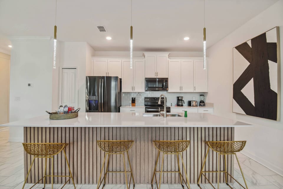 Welcome to a spacious kitchen with sleek white cabinetry and a stunning marble island, perfect for casual meals on stylish gold bar stools.