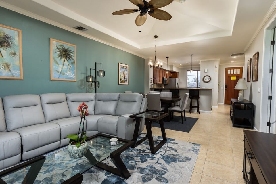 - Open concept living area with sectional sofa and view into dining and kitchen spaces - Ceiling fan and pendant lights enhance comfort and style throughout the space - Decor blends tropical accents with modern furnishings for a cozy inviting feel