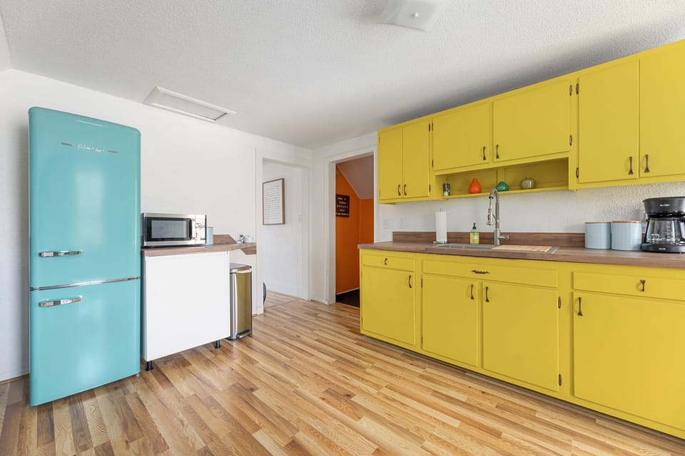 Cheerful kitchen w/ vibrant yellow cabinets, retro fridge & wood-look floors