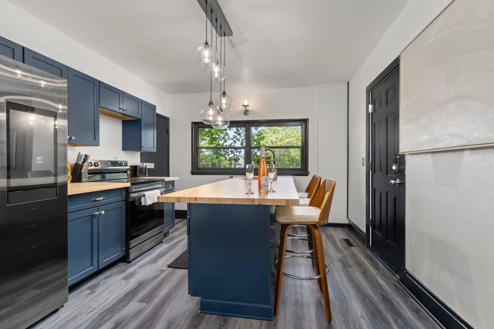 Sleek kitchen w/ blue cabinets, island seating & wide window bringing in natural light