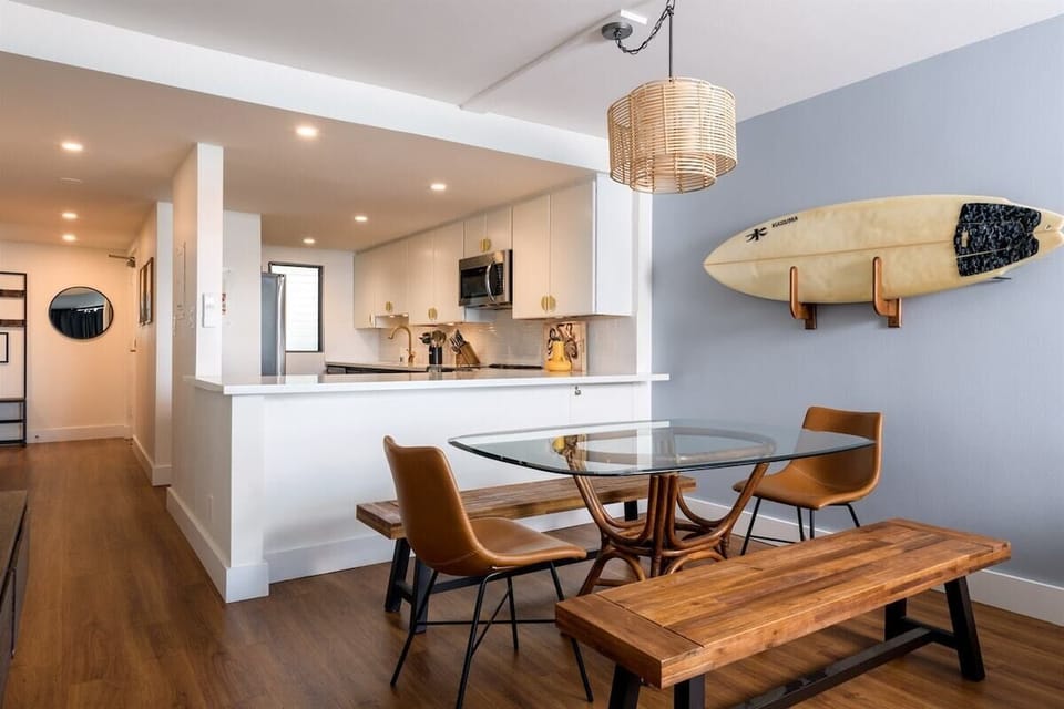 Chill surfer vibes meet modern style—glass table, leather chairs, and a surfboard on the wall. Clean, cool, and beachy. 
