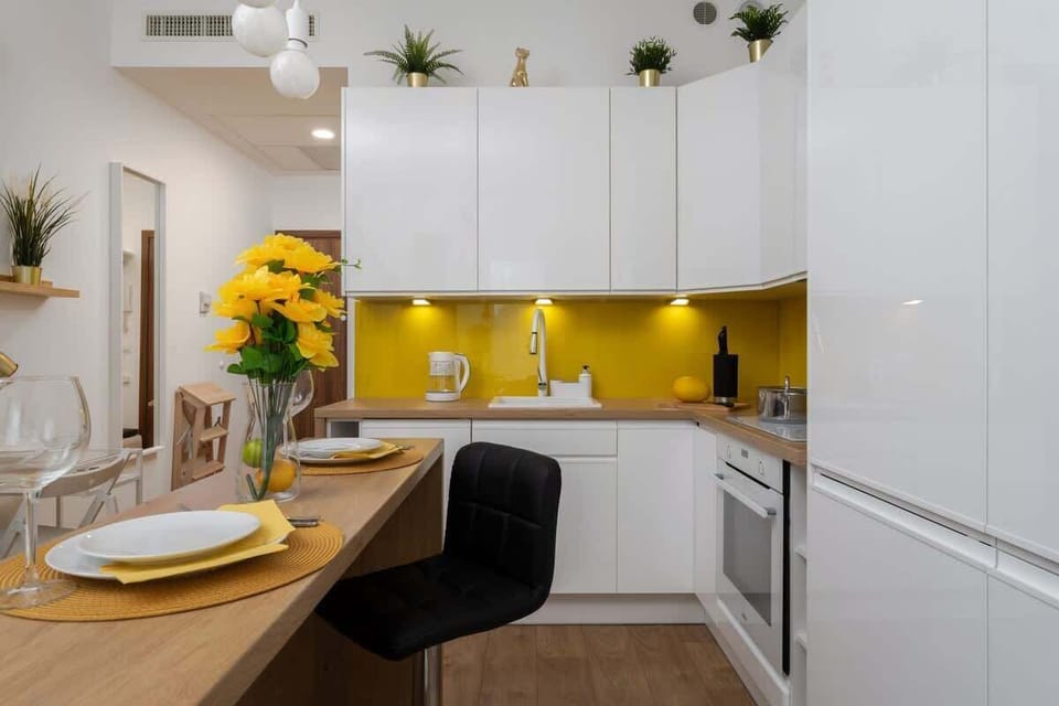 The kitchen area reveals sleek white cabinetry, yellow accents, and a built-in oven with plenty of counter space.