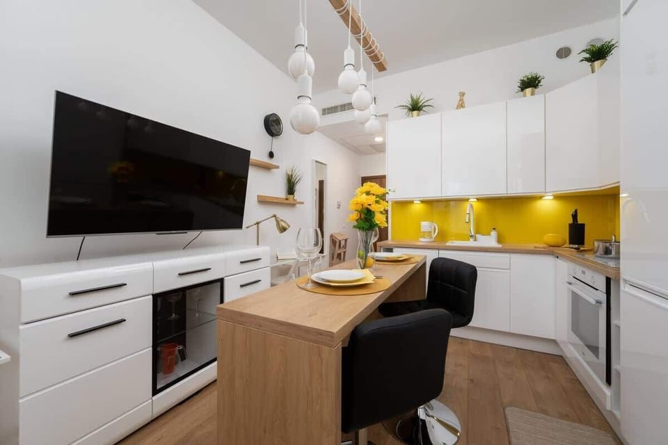  A modern kitchenette with sleek white cabinets and a bright yellow backsplash creates a cheerful atmosphere.