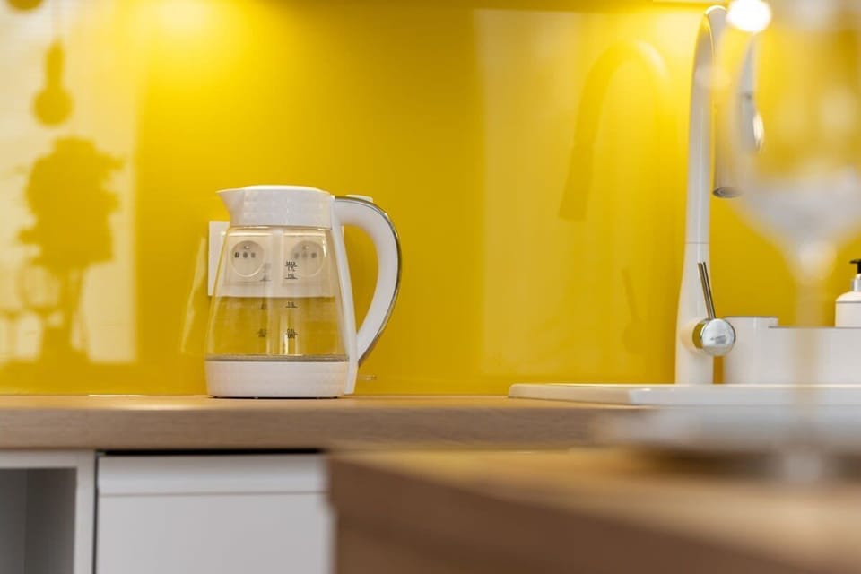 A close-up of the countertop shows a white coffee maker and electric kettle against the bright yellow backsplash.