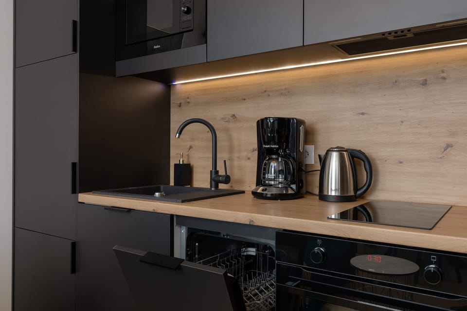 A modern kitchen with sleek black cabinets, wooden countertops, and integrated appliances. The design is clean and contemporary, emphasizing functionality.