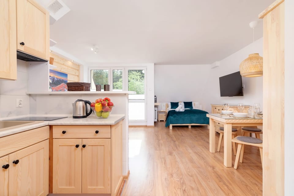 An open-plan living space combining a seating area with a kitchenette and dining space, featuring wood accents and a comfortable layout.