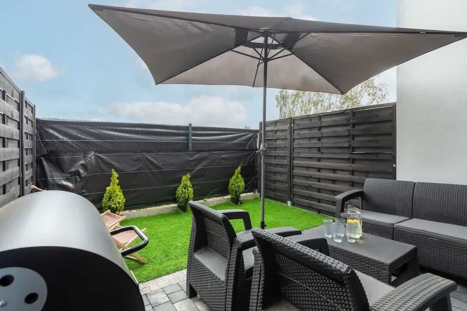 A private patio with outdoor furniture, a green lawn, and umbrellas for enjoying sunny days.