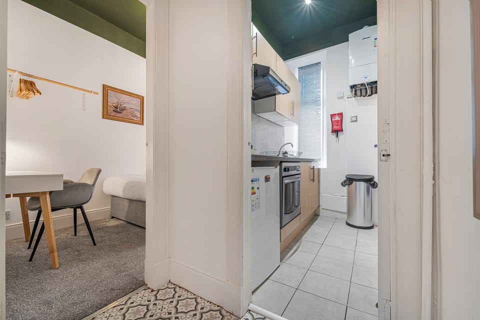Bright view into the apartment’s compact kitchen with modern appliances and natural light, alongside a cosy workspace and bedroom area just off the hallway.