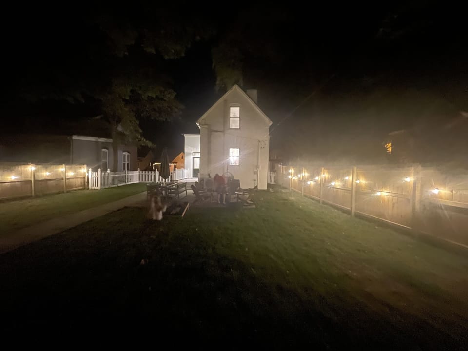 Backyard area with fire pit, rocking Adirondack chairs, dining and corn hole set