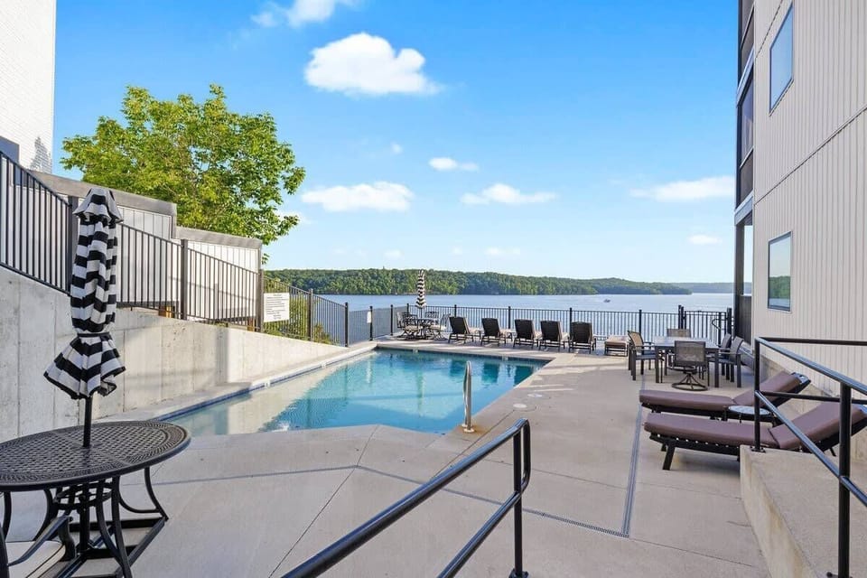 Beautiful waterfront pool area with a spacious patio, outdoor seating, and scenic views of the surrounding lake.