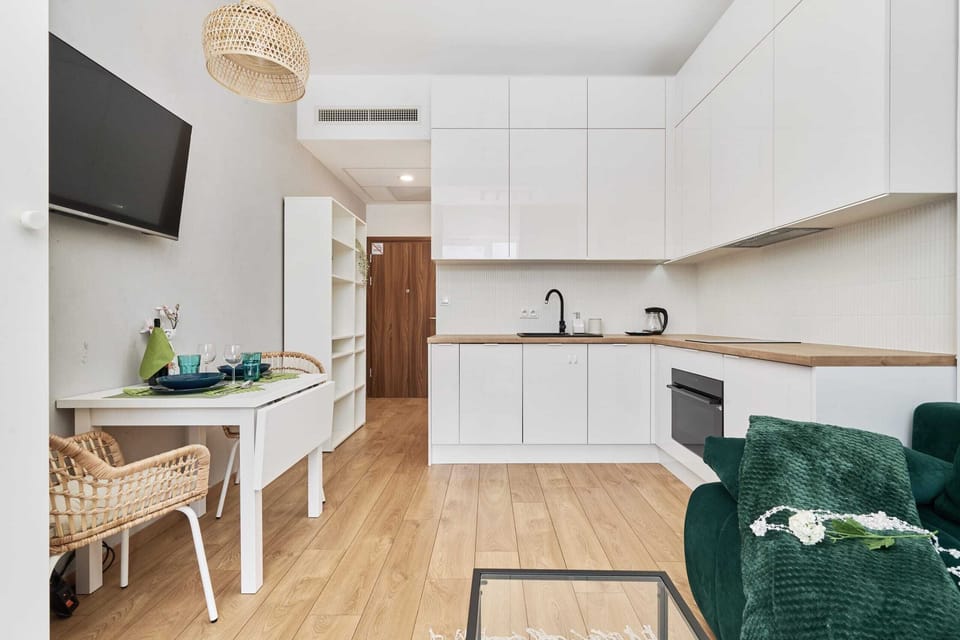 A modern, white kitchen with wooden flooring leading into the living room.