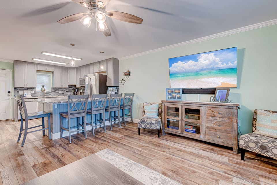 Relax in your coastal-inspired living space with modern kitchen, cozy seating, and large TV for perfect vacation evenings together.