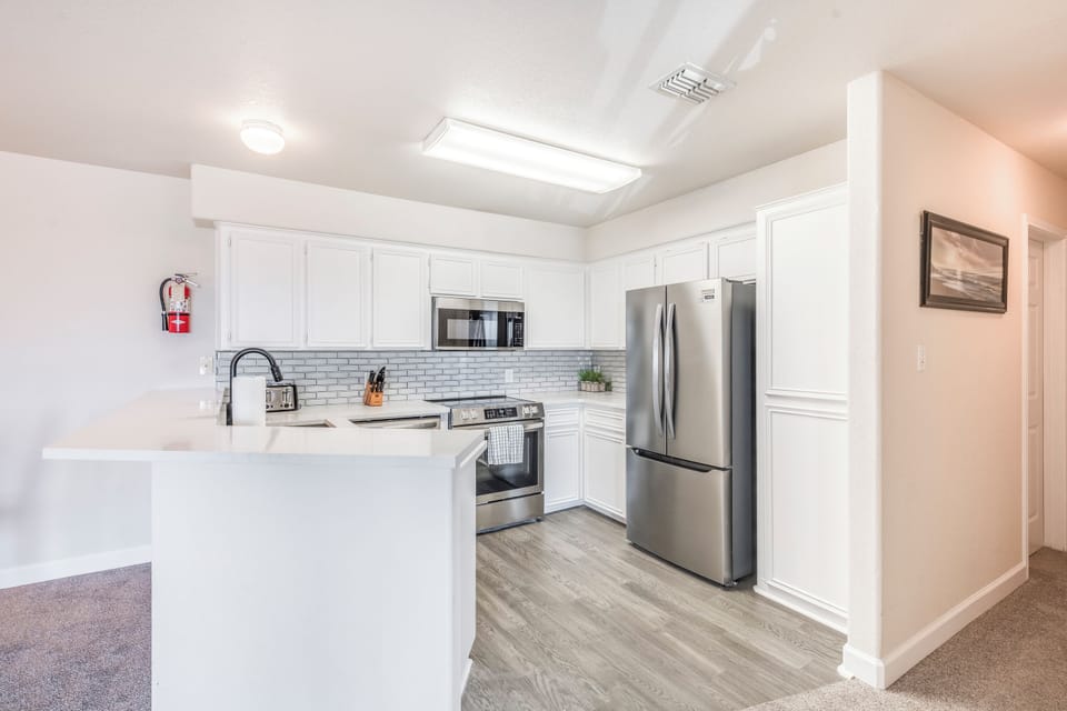 Your fully equipped kitchen features modern stainless steel appliances and pristine white cabinets, perfect for preparing memorable meals during your stay.