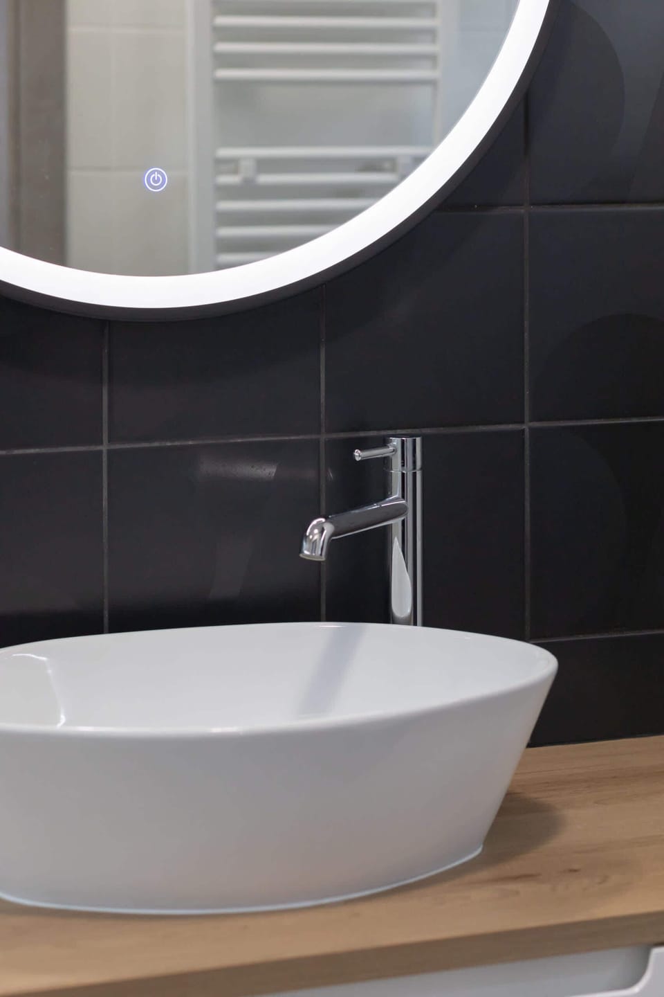 A close-up of a minimalist basin and round mirror, paired with a dark tile background for an elegant look.