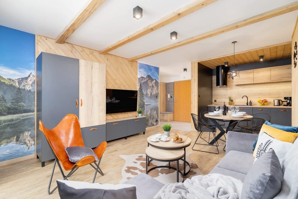 A spacious living area with an armchair and sofa around a central coffee table, decorated with soft furnishings.