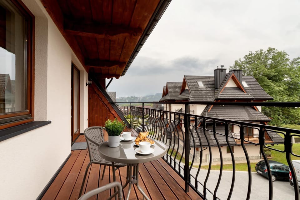A wooden balcony with outdoor seating overlooking the chalet-style buildings and surrounding greenery.