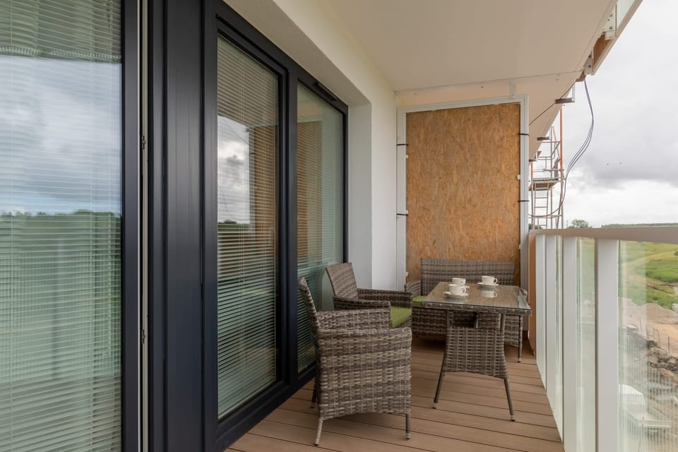 A private balcony with wicker chairs and a glass railing, offering scenic views of green fields.