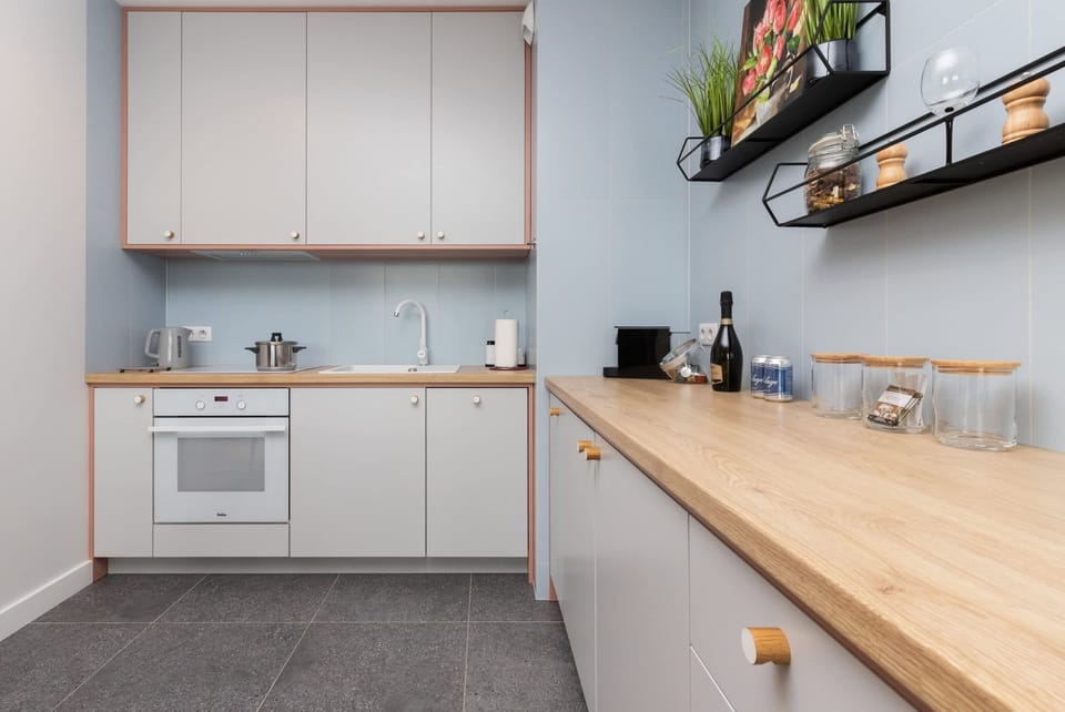 A sleek kitchen featuring white cabinetry, shelves with decorative items, and ample counter space. The setup appears bright and functional.