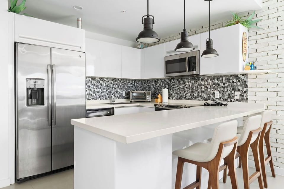 Your bright, modern kitchen features sleek appliances, a spacious island with seating for four, and stylish pendant lighting—perfect for cooking meals or sharing morning coffee together.