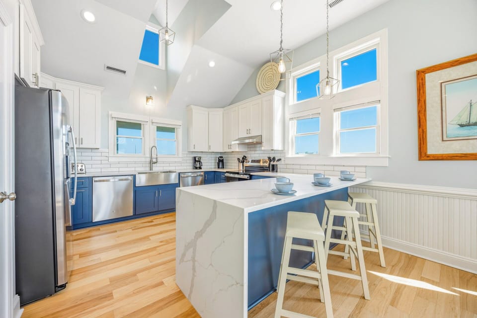 Step into your fully equipped kitchen, where soaring ceilings and abundant natural light create an inviting space for preparing meals together. The nautical-inspired blue cabinets and marble island add coastal charm to your home away from home.