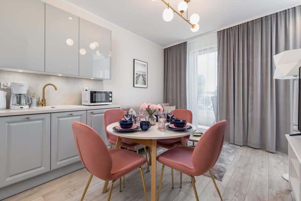 A dining area adjacent to a minimalist kitchen, with a round table and pink chairs.