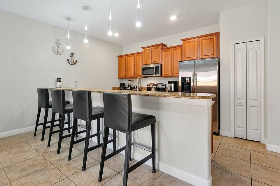 Enjoy a stylish kitchen featuring rich wooden cabinets and sleek stainless steel appliances. The spacious island, with modern high-backed chairs, creates an inviting space for casual dining and lively conversations in a bright.