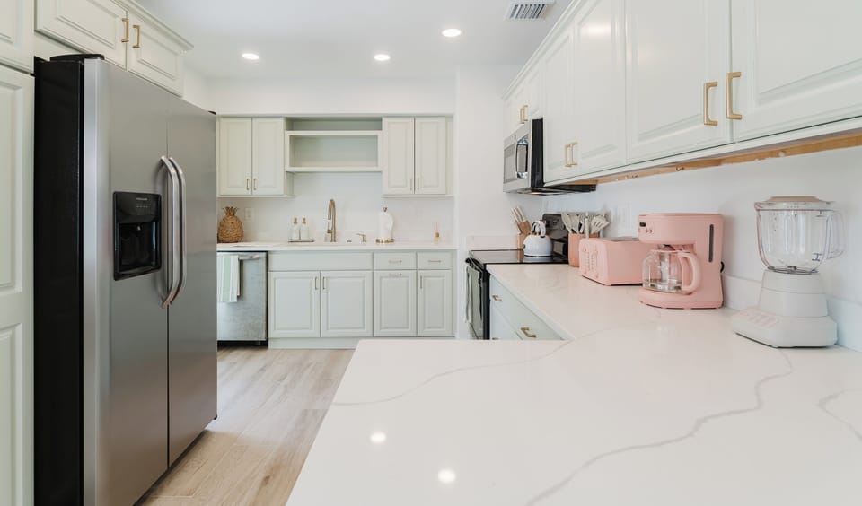 A beautifully updated kitchen designed with style and function in mind, offering elegant sage cabinetry, quartz countertops, champagne gold fixtures, a farmhouse sink, stainless steel appliances, and premium small appliances for your stay.