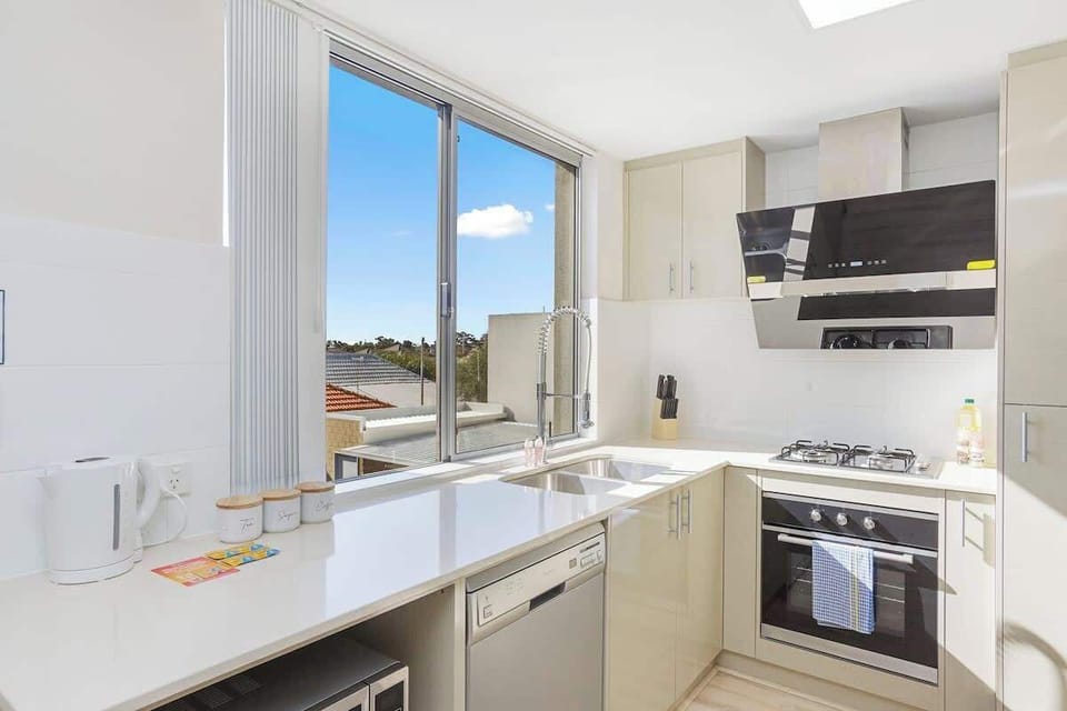 Bright, modern kitchen with a view! Includes window, sink, oven, stovetop, rangehood, kettle, microwave, dishwasher, and ample cabinetry for your perfect stay.