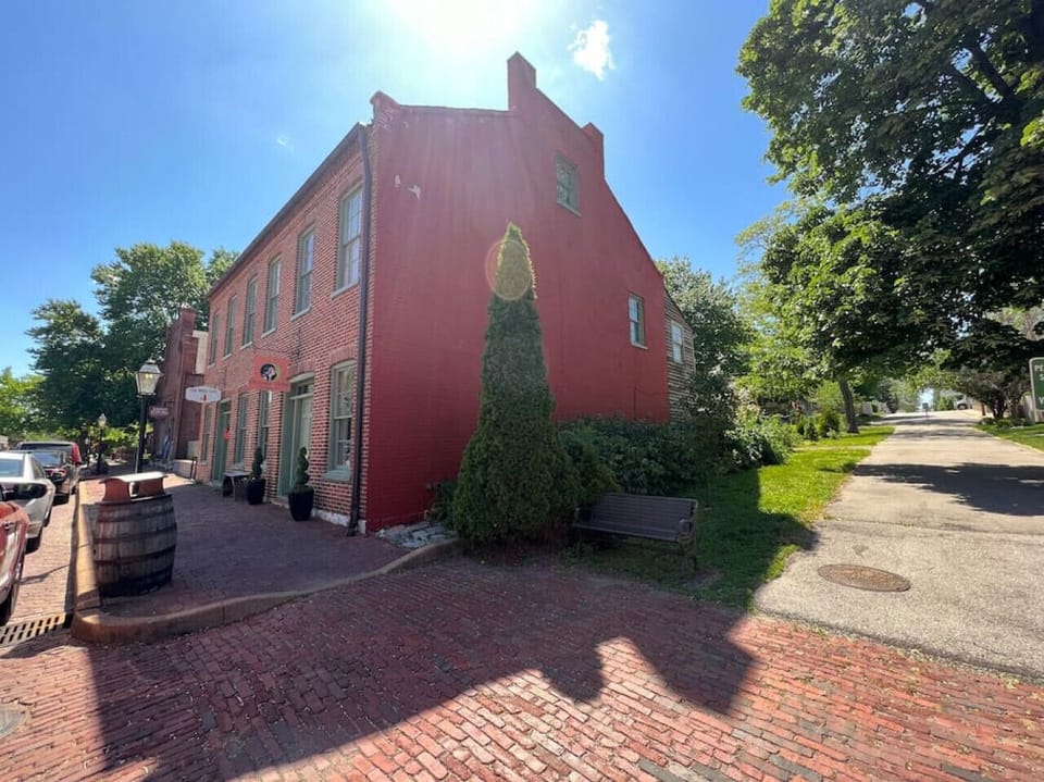 Daytime street view of a red-brick historic building with storefront windows, a stepped gable, brick paving, trees, and a side lane.