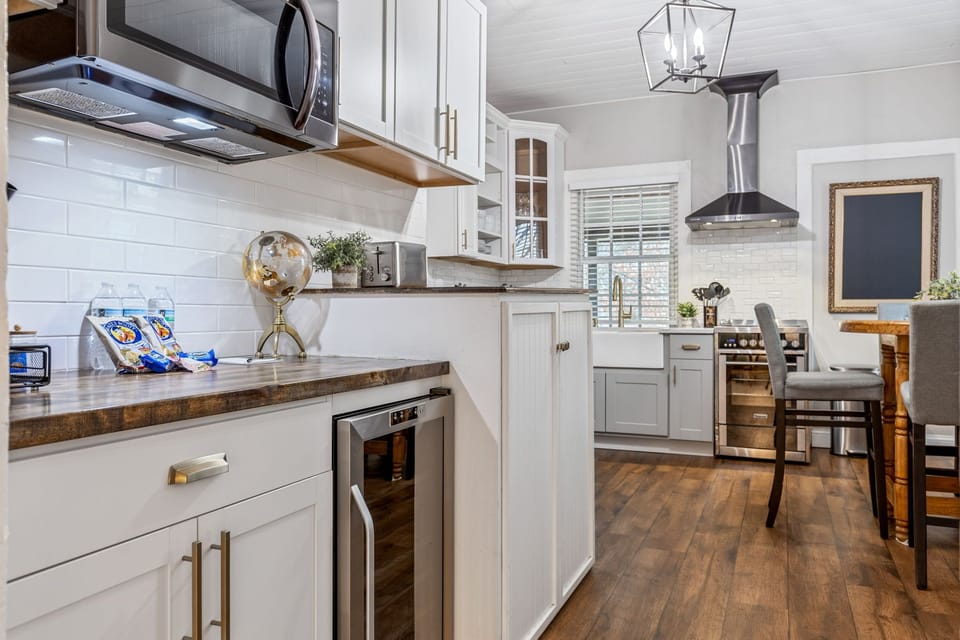 Wide kitchen view with white cabinetry, stainless microwave and range, farmhouse sink, long counter and adjoining dining table.