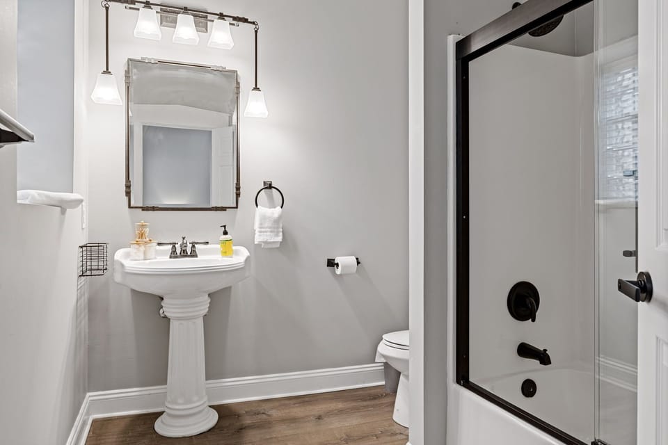 The convenient half bathroom includes a pedestal sink, toilet, mirror, and bright neutral finishes.