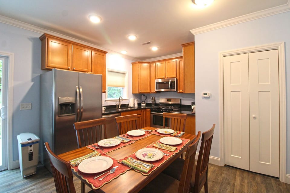 Dining table set for guests beside a fully equipped kitchen with stainless steel appliances and wood cabinetry. Ideal for family meals during a Bryson City getaway.