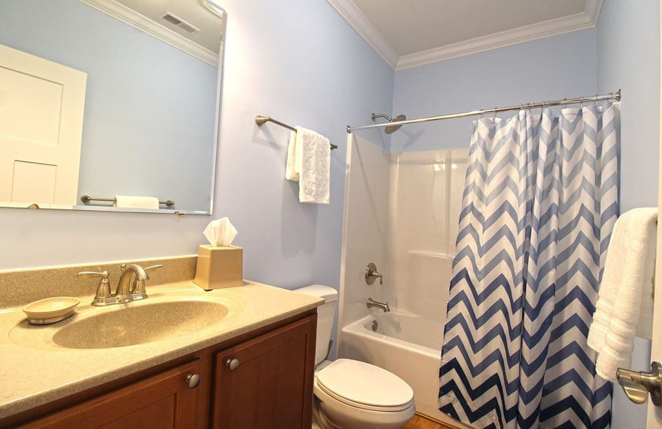 Full bathroom with single vanity, tub and shower combination, patterned shower curtain, and fresh towels. Convenient bathroom for guests staying in Bryson City.