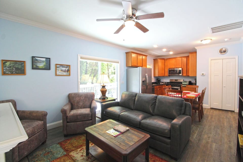Open concept living room with leather seating, ceiling fan, and adjoining kitchen with wood cabinetry. Located near downtown Bryson City for easy access to local attractions.
