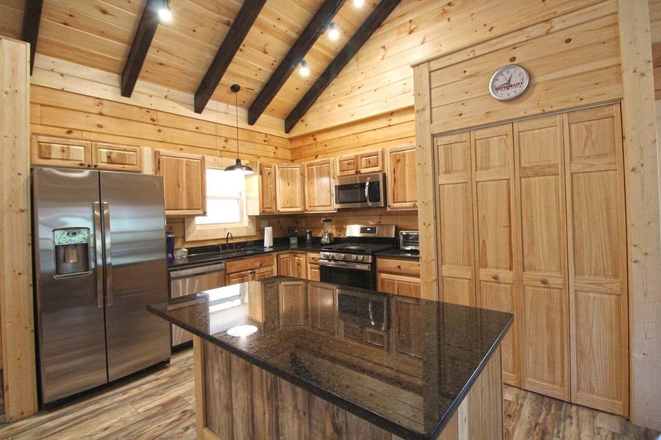 Kitchen featuring granite island countertops, natural wood cabinetry, and stainless-steel appliances. Modern cooking space within this Bryson City cabin rental.