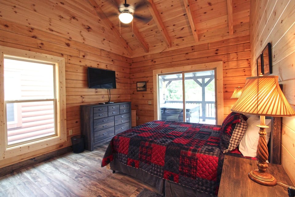 Bedroom featuring a king bed, wood-paneled walls, dresser, television, and large window. Located within a Bryson City cabin rental.