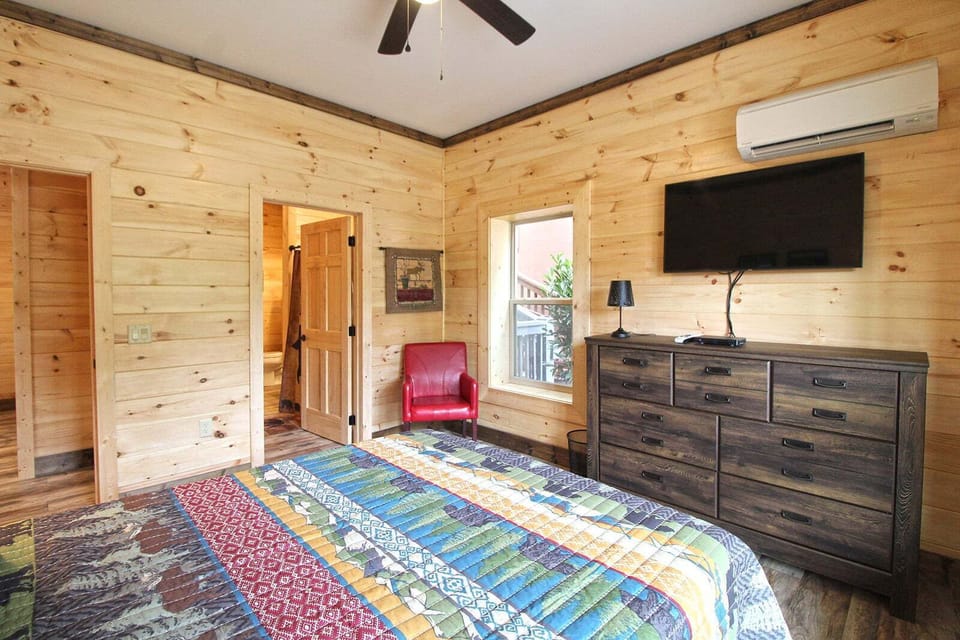 Corner bedroom perspective featuring dresser storage, television, red chair, and doorway leading to additional cabin spaces. Comfortable lodging in Bryson City.