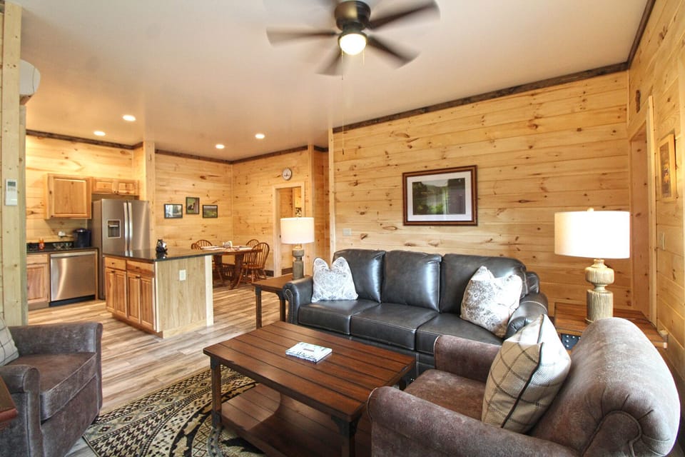 Living room featuring leather sofa, coffee table, lamp, and kitchen visible beyond. Convenient cabin rental in Bryson Village.