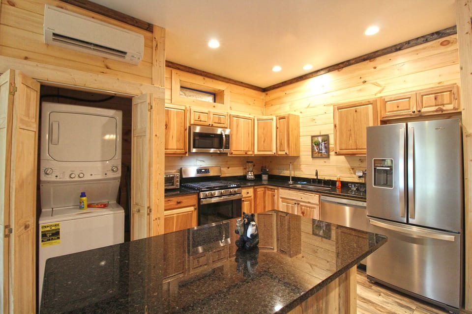 Kitchen view including granite counters, stainless refrigerator, wood cabinets, and adjacent laundry area. Convenient pet-friendly cabin rental in Bryson City.
