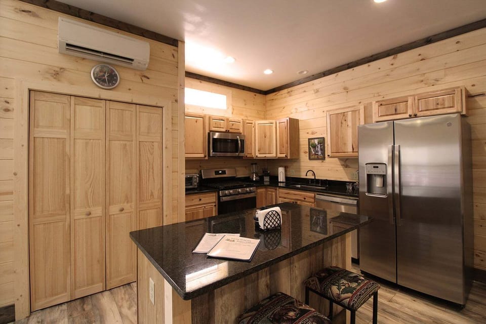Kitchen featuring granite island, wood cabinetry, and stainless-steel appliances. Well-equipped cabin kitchen in downtown Bryson City.
