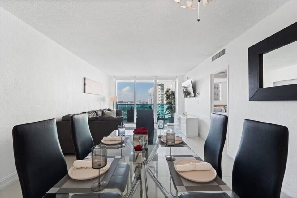Elegant dining room with modern glass table seating 6 guests, contemporary black chairs, and sophisticated lighting. Perfect for family meals and special occasions with ocean views nearby.