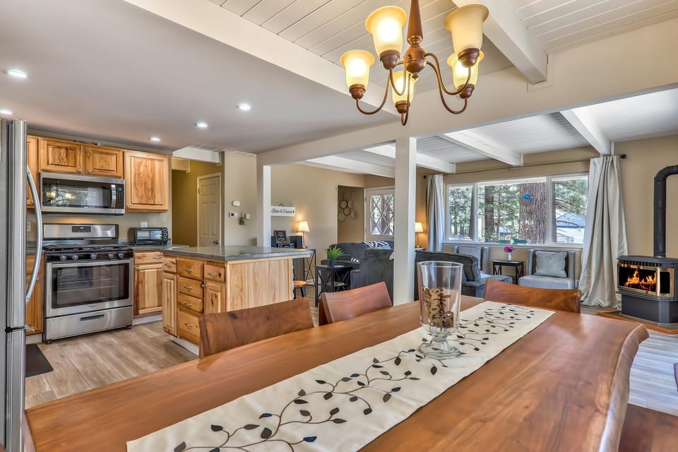 Wood dining table with leaf-patterned runner sits near open kitchen featuring natural wood cabinets and stainless appliances.