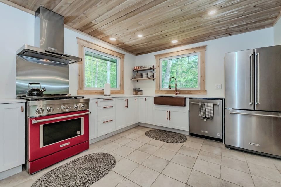 Cook with a view! This fully-equipped kitchen features large awning windows, a bold red stove, and everything you need for meals at home.. 