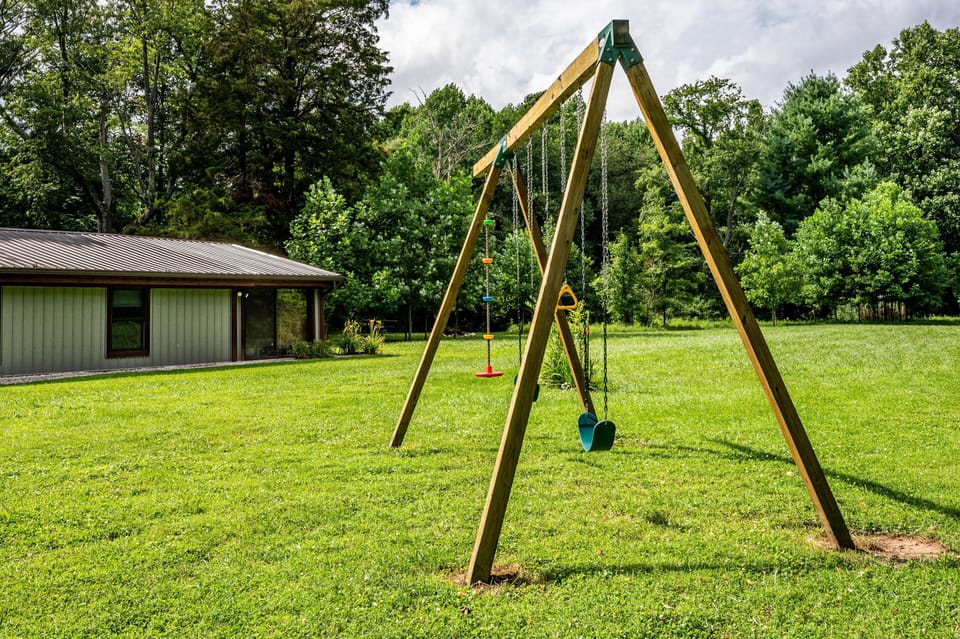 Wood-frame swing set with colorful seats stands on a green lawn beside the metal-roofed cottage.