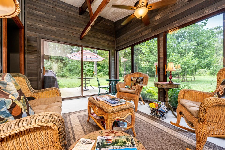 Screened-in porch with wicker seating, patterned cushions, ceiling fan, and sliding glass doors to patio.