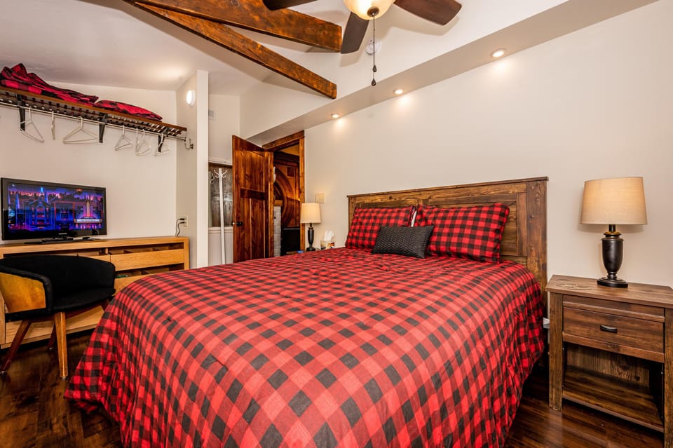 Barn-style bedroom with dark hardwood floors, red plaid bedding, wood furniture, and ceiling fan.