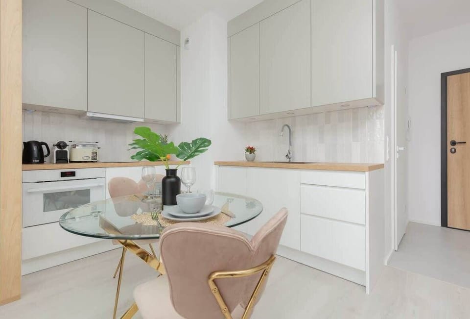 A kitchen with white cabinetry, wooden accents, and a round dining table paired with elegant green chairs, blending functionality with stylish design.