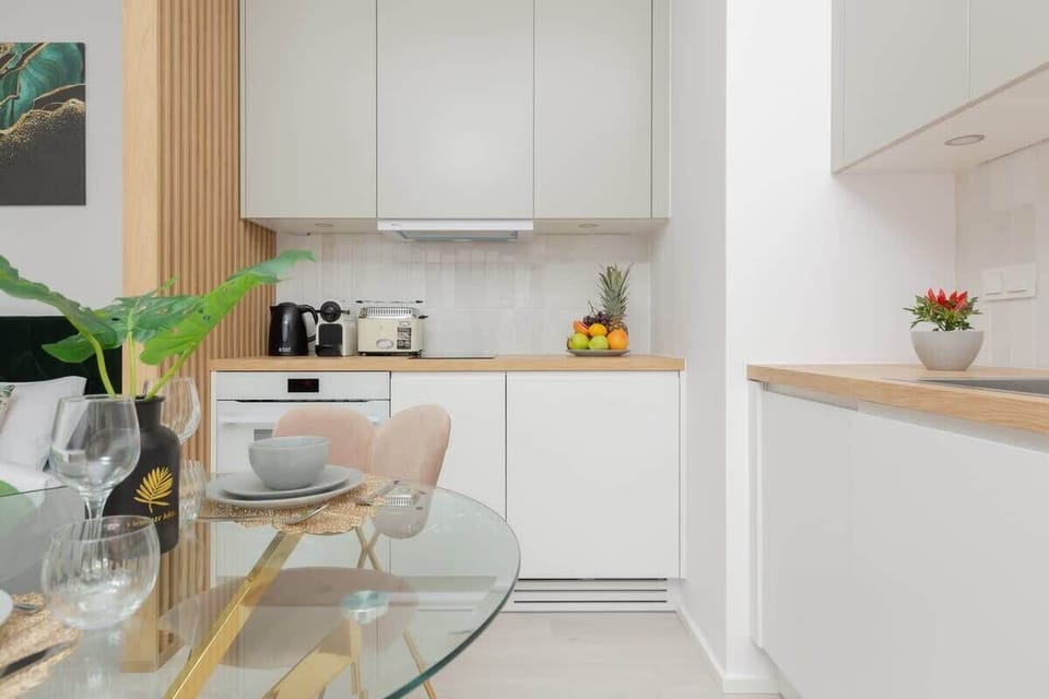 A kitchen with white cabinetry, wooden accents, and a round dining table paired with elegant green chairs, blending functionality with stylish design.